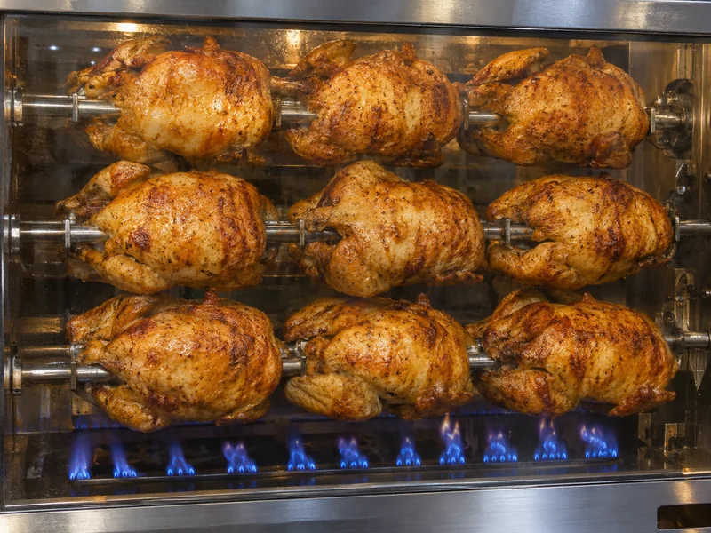 Pollos girando en el asador de gas con las llamas azules al fondo